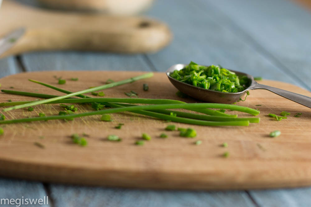 Fresh chopped chives in a tablespoon sitting on a cutting board.