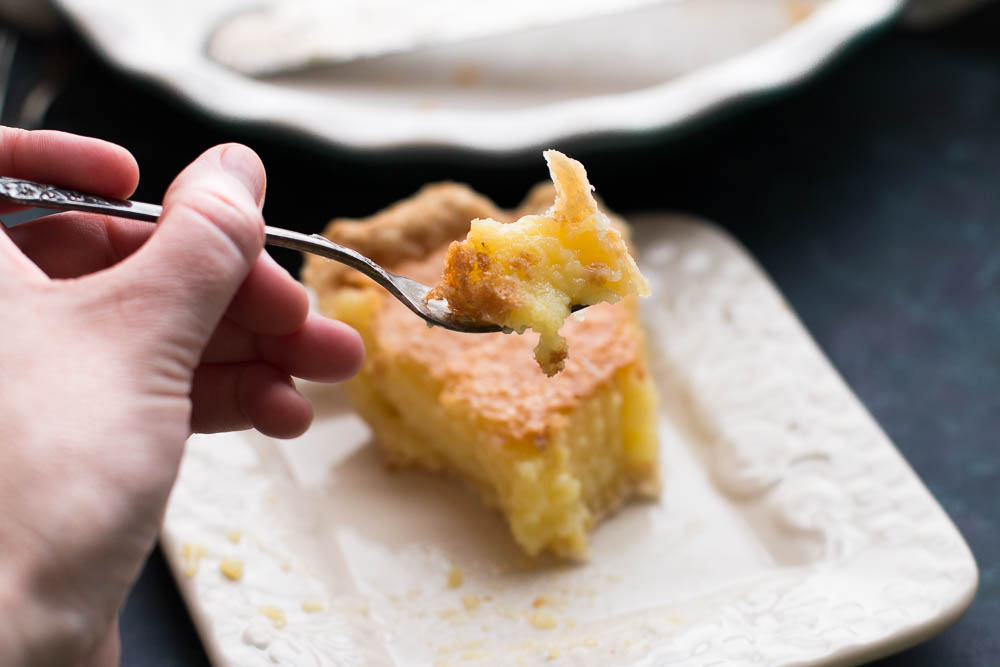 Close up shot of a hand holding a fork with a bite of lemon chess pie on it.