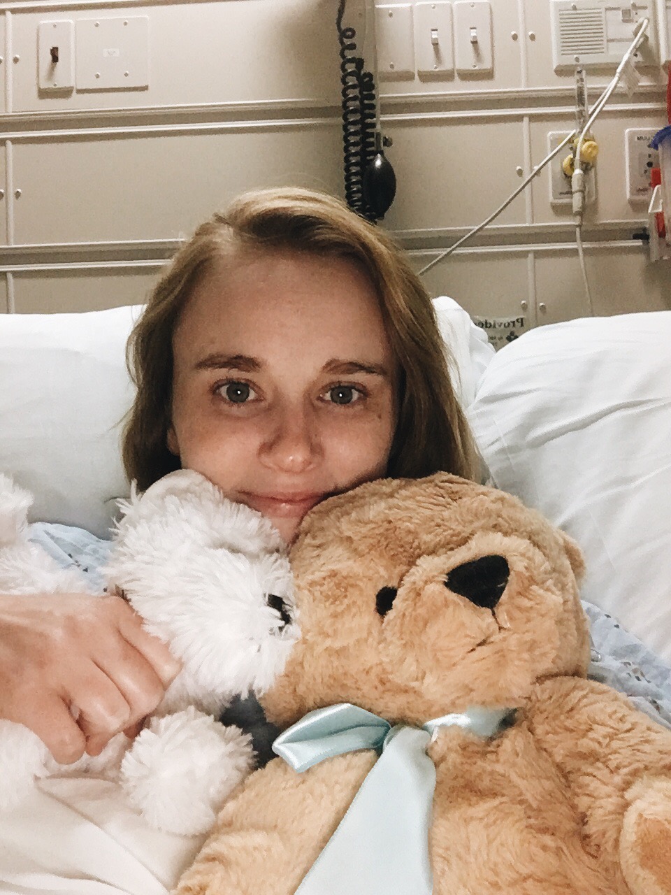 Picture of the author, Megan, in a hospital bed holding two stuffed animals.