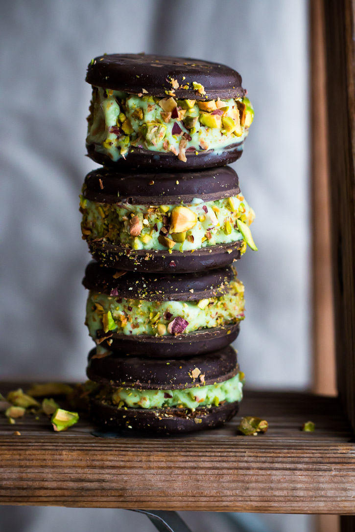 A close up vertical side shot of 4 pistachio ice cream sandwiches stacked on top of each other.
