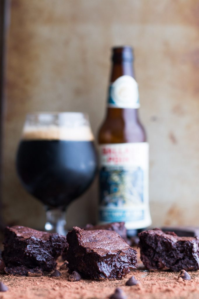 Vertical shot of Fudgy Beer Brownies in front of a goblet glass filled with beer next to a beer bottle.