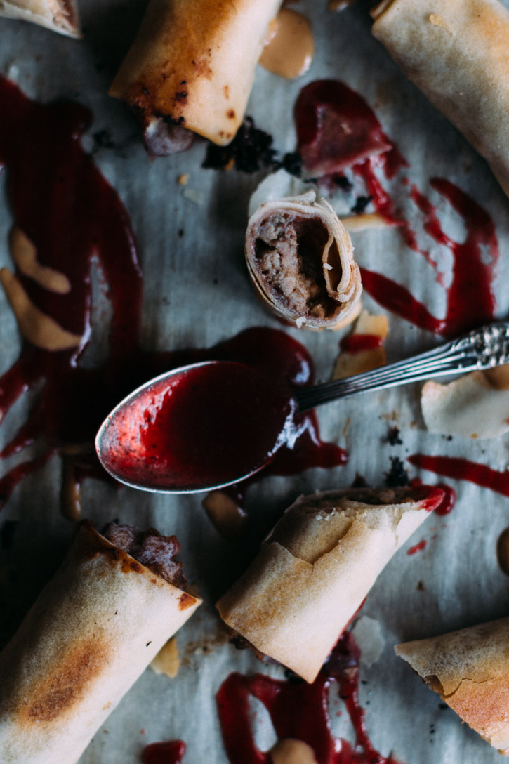 baked Duck Spring Rolls laid out on a parchment covered baking sheet with a spoon and peanut and plum sauce splattered everywhere