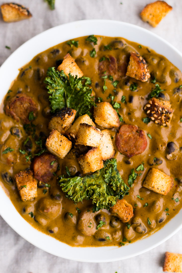 Croutons and kale chips piled on top of a bowl of Creamy Red Pepper and Andouille Sausage Soup.