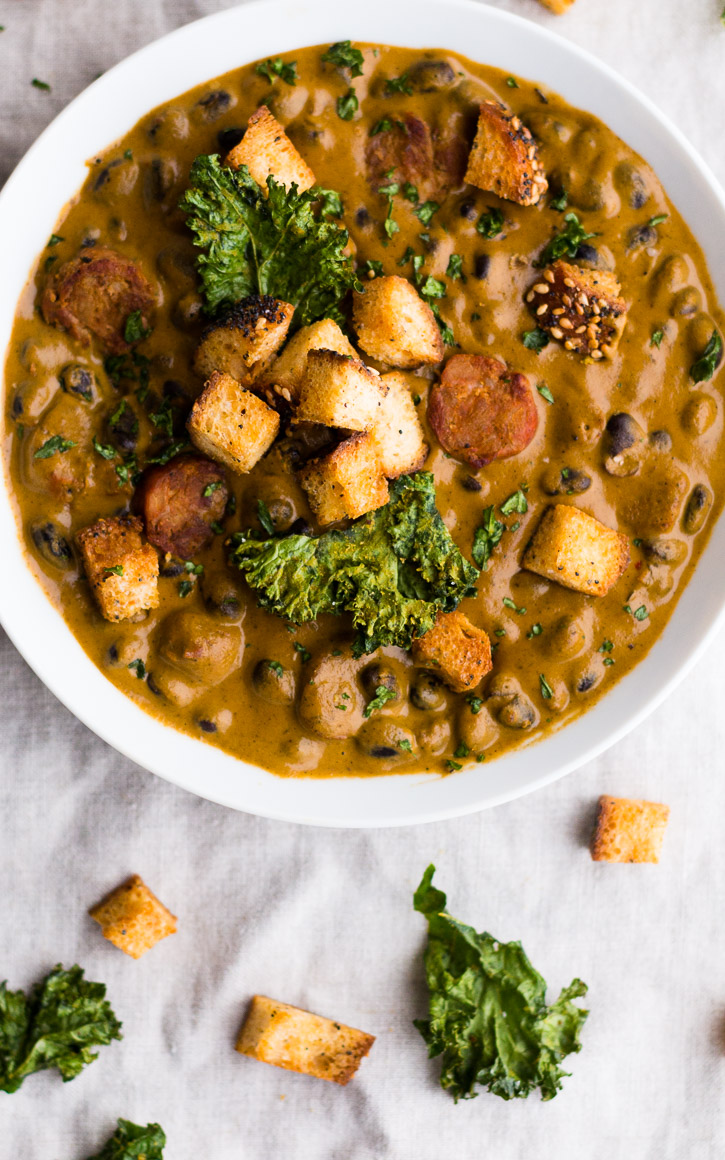 Creamy Red Pepper and Andouille Sausage Soup with croutons piled on in the middle with two kale chips.