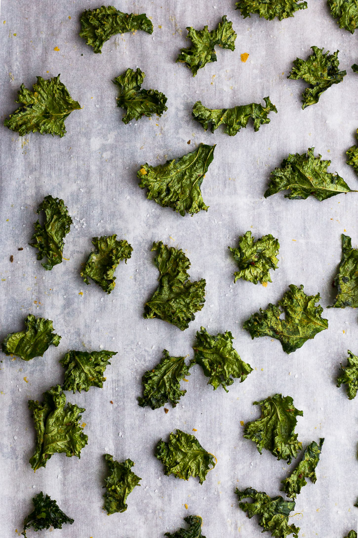 Crispy baked kale chips laid out on a parchment paper covered baking sheet.