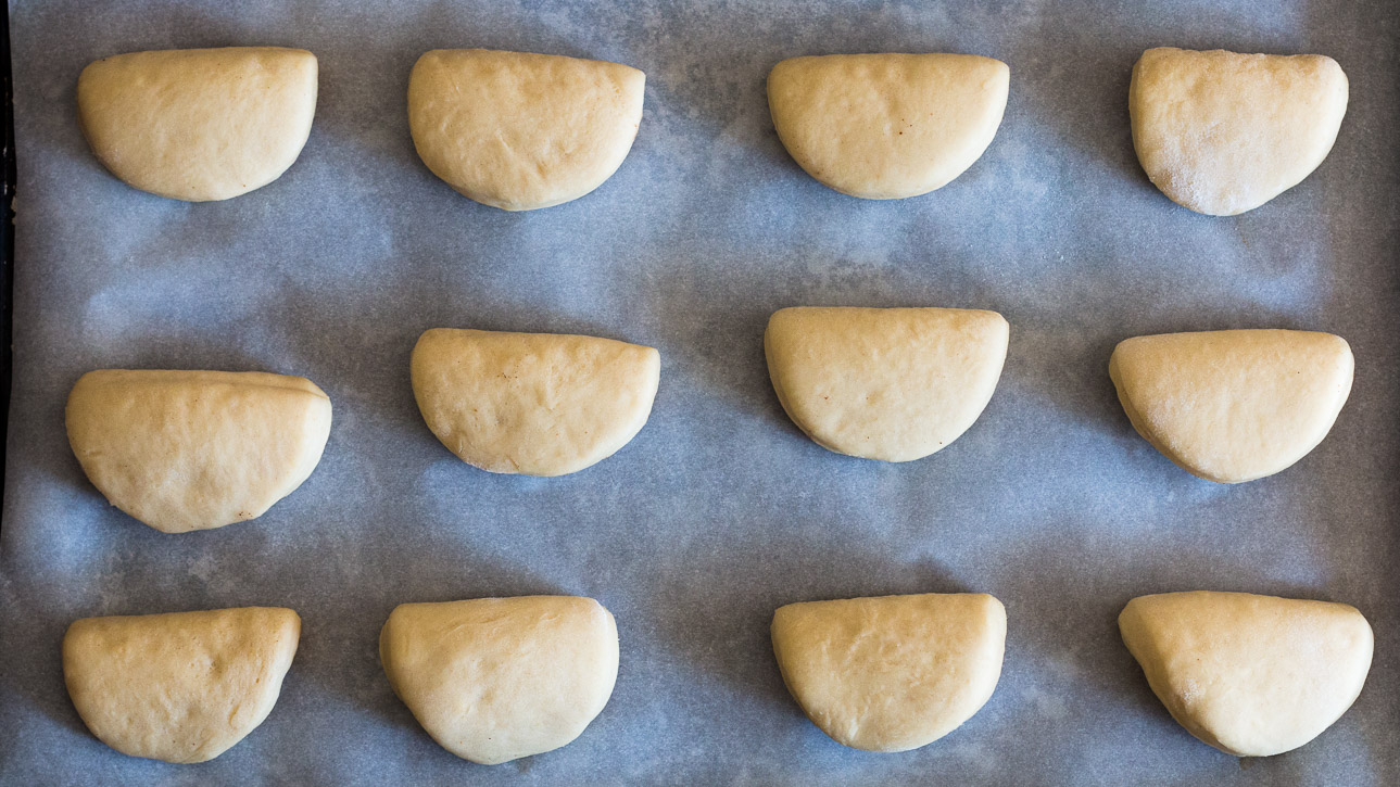Folded dough rounds placed on a parchment covered baking sheet in rows.