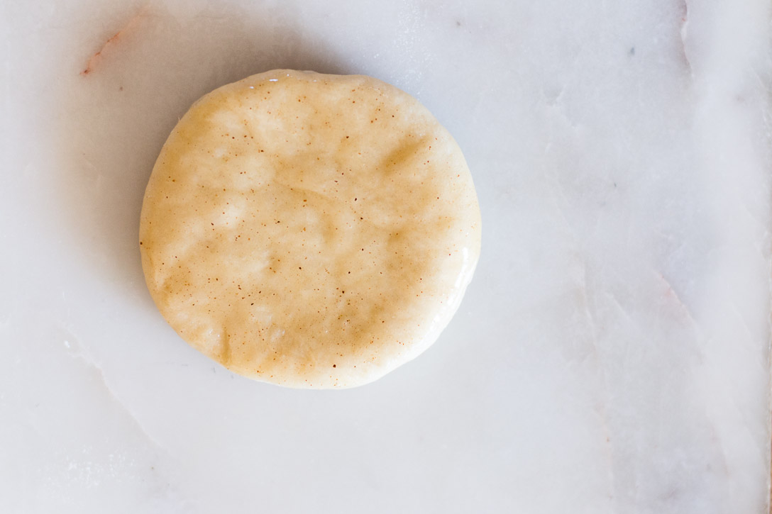 A close up of a cut circle of dough covered with brown butter on a marble surface.