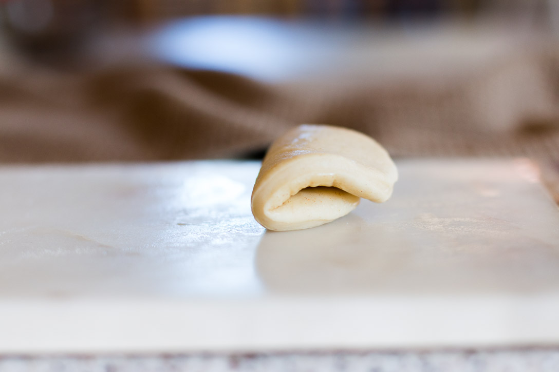 Side view of a circle of dough folded over in half on a marble cutting board.