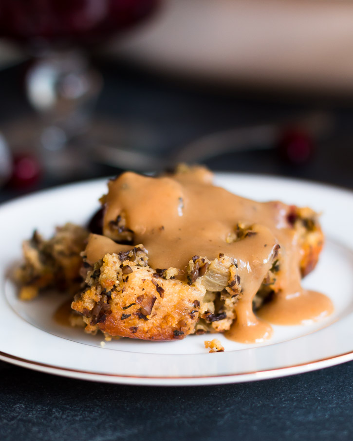 Close up side view of Cornbread and Cranberry Vegetarian Stuffing covered in Vegetarian Mushroom Gravy on a plate.