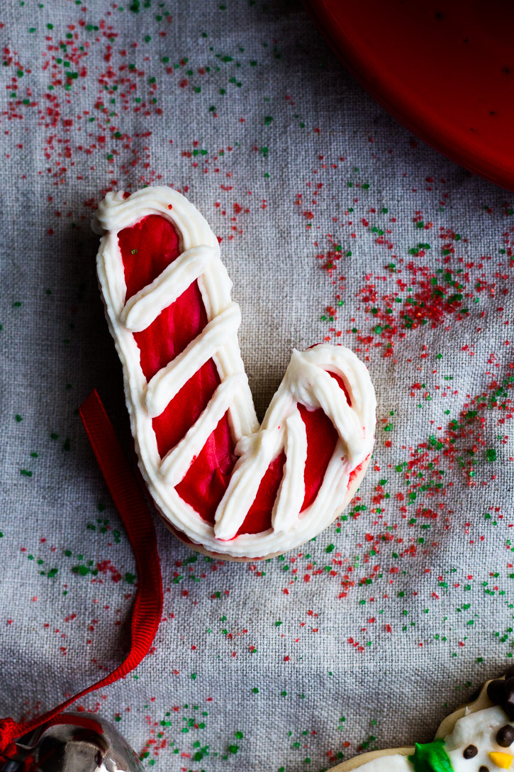 Frosted candy cane shaped cookie on a sprinkle covered clothe background.