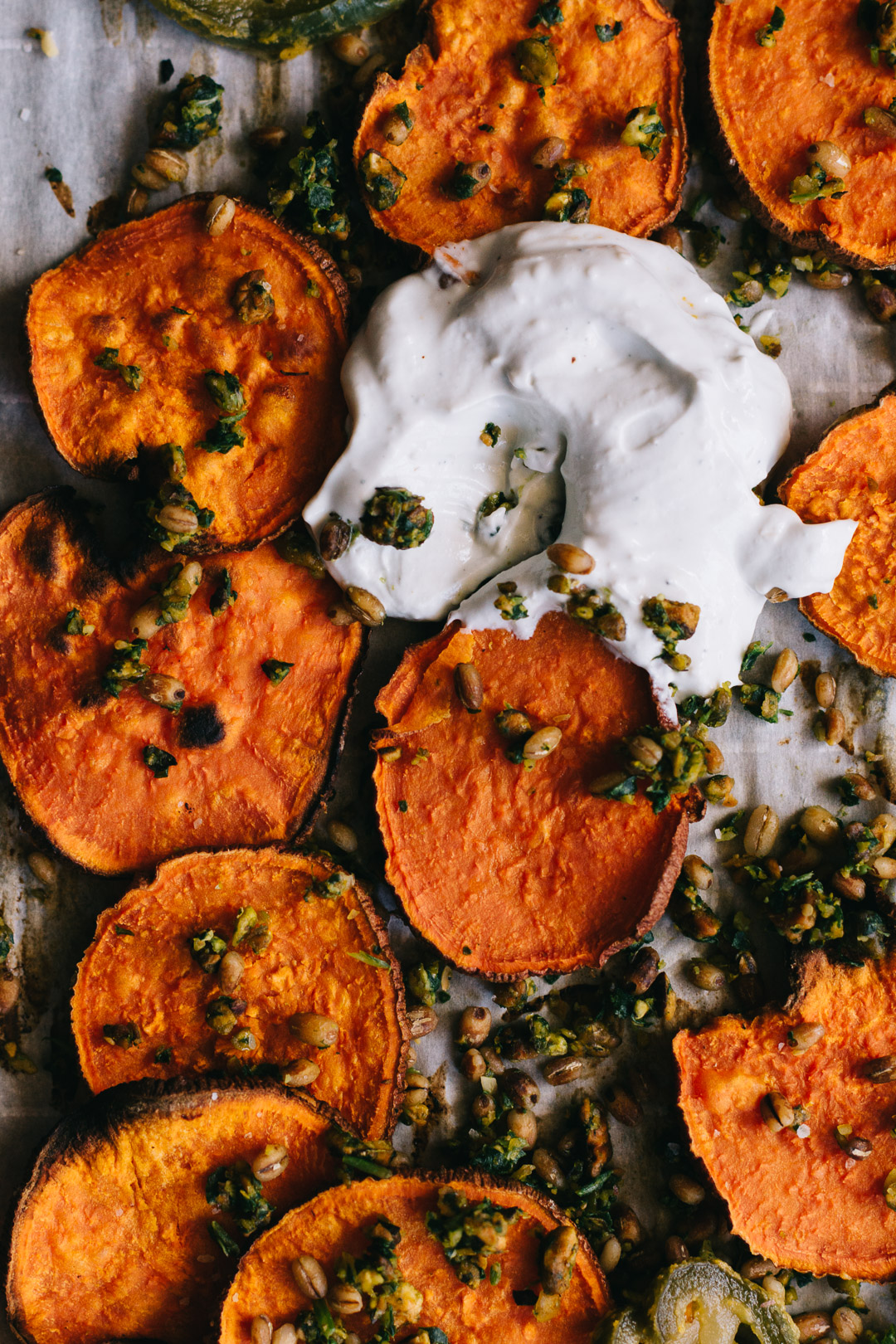 Close up overhead shot of a dollop of sour cream blue cheese dip on a parchment paper covered baking sheet surrounded by sweet potato crisps, gremolata, and barley.