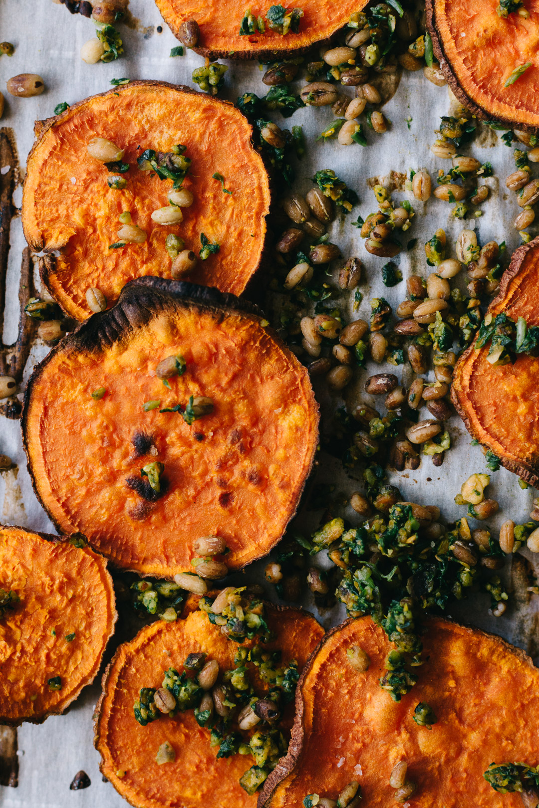 Close up overhead shot of baked sweet potato crisps and gremolata with barley on a parchment paper covered baking sheet.