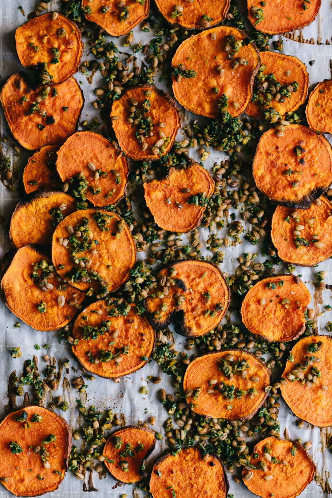Overhead shot of baked sweet potato crisps and gremolata with barley on a parchment paper covered baking sheet.