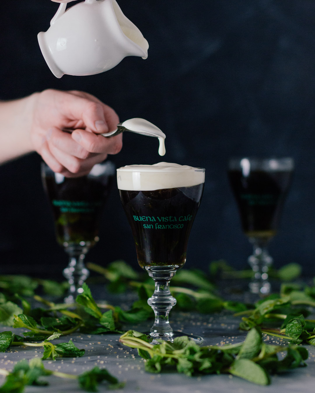 Vertical shot showing a hand pouring cream into an Irish Coffee glass.