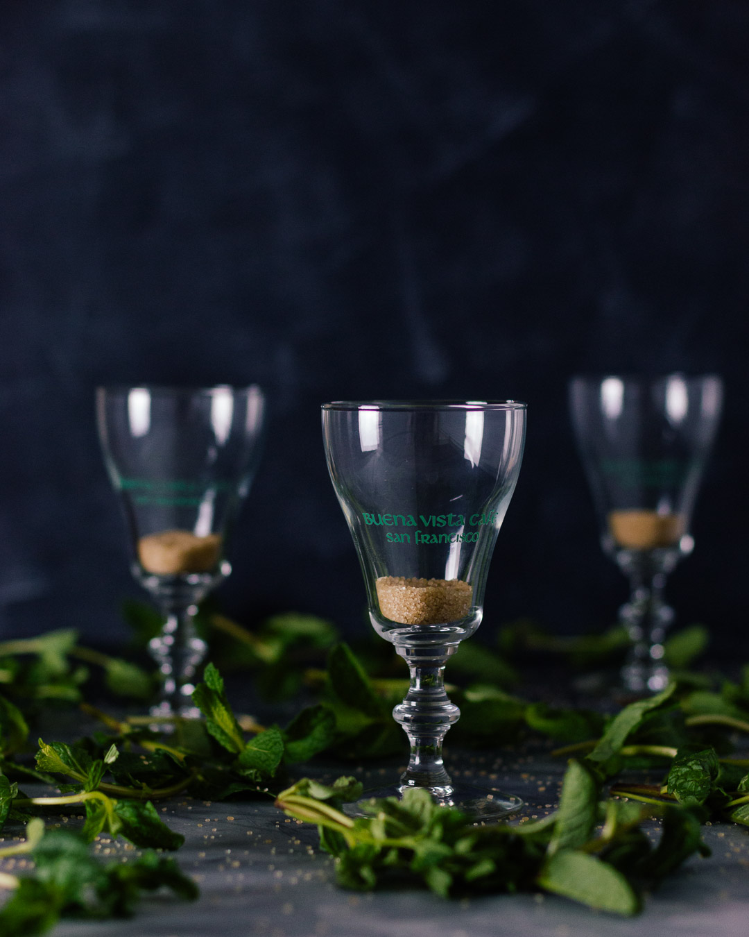 Vertical side shot of three Buena Vista Irish Coffee goblet glasses with sugar in them.