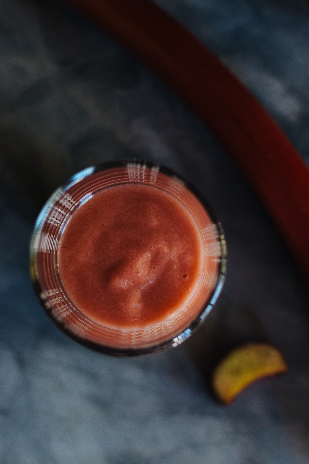 An overhead shot of rhubarb puree in a shot glass surrounded by a stalk of rhubarb.
