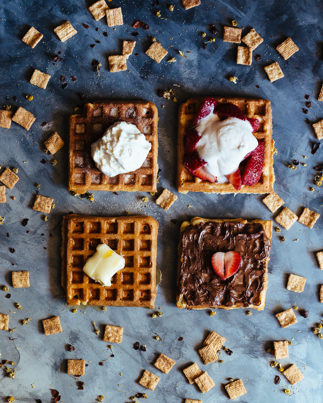Overhead shot of four waffles with different toppings on them and surrounded by cinnamon toast crunch cereal. 