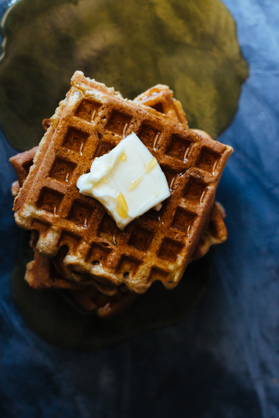 Overhead shot of a stack of waffles with a pat of butter on top and drizzled with maple syrup.