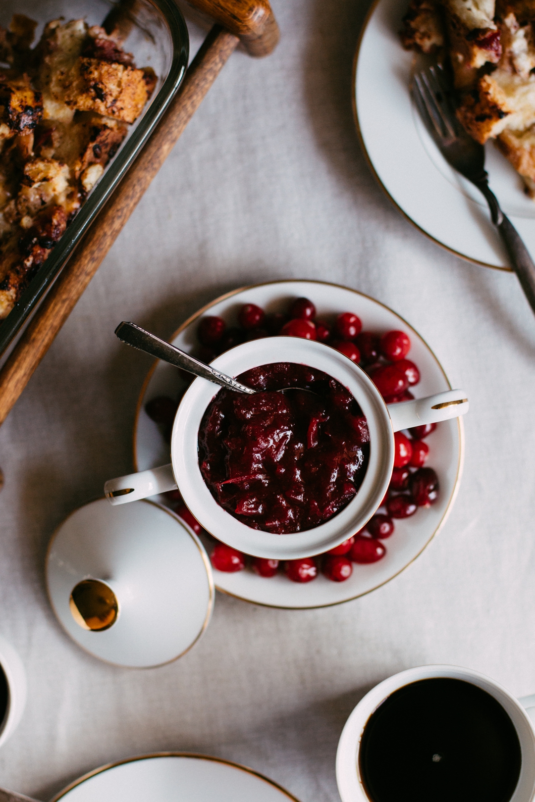 Overhead shot of ginger pear cranberry sauce in a two handle sugar jar with a spoon in it on a plate surrounded by cranberries.