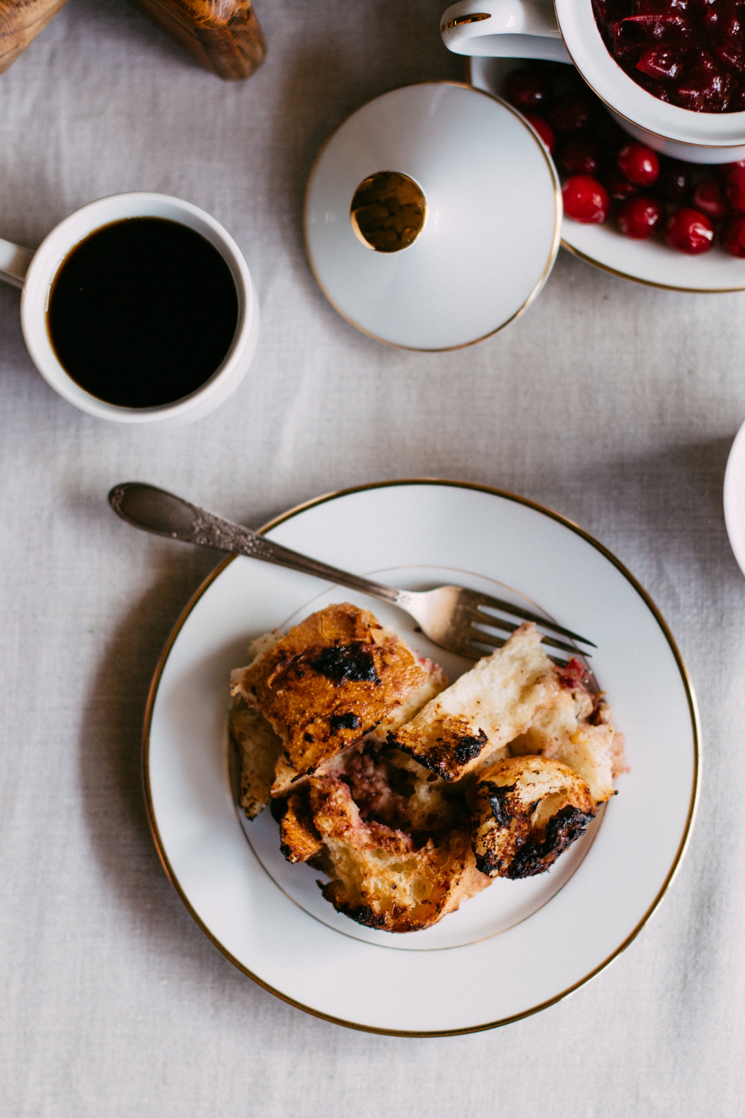 Overhead shot of a serving of savory French toast casserole on a plate surrounded by a coffee cup and cranberry sauce.