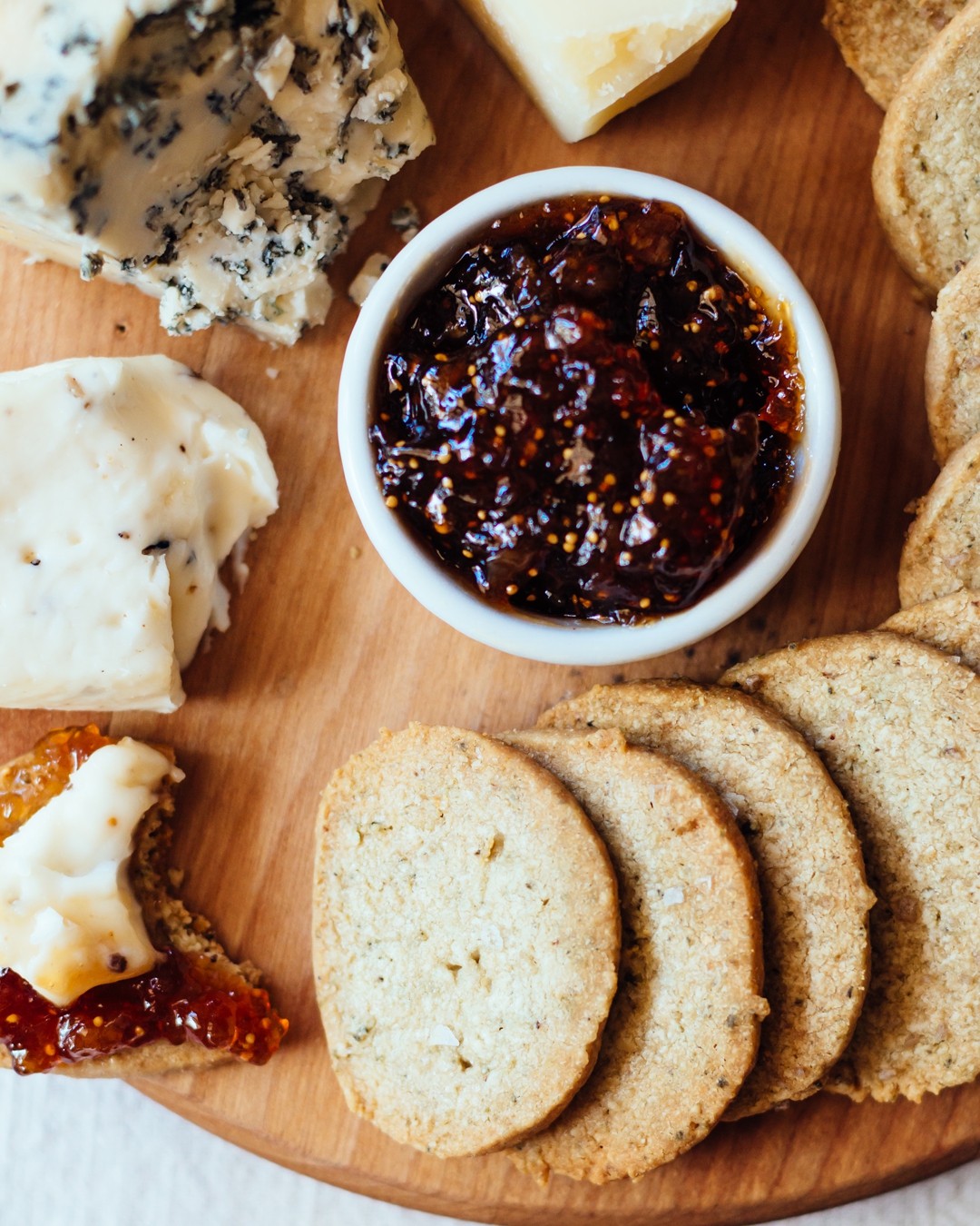 Close up overhead shot of pumpkin seed biscuits on a wooden surface surrounded by cheese and fig jam.