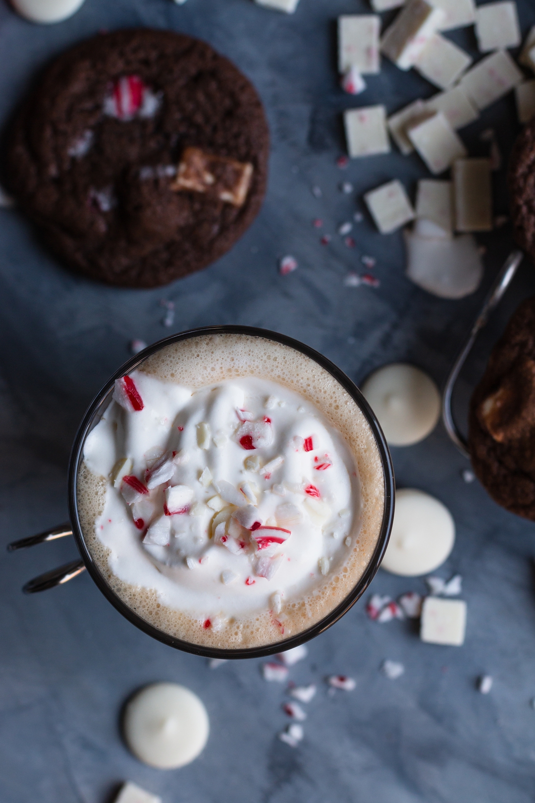 Close up overhead shot of a latte surrounded by white chocolate, crushed candy canes, peppermint chips, and a cookie.
