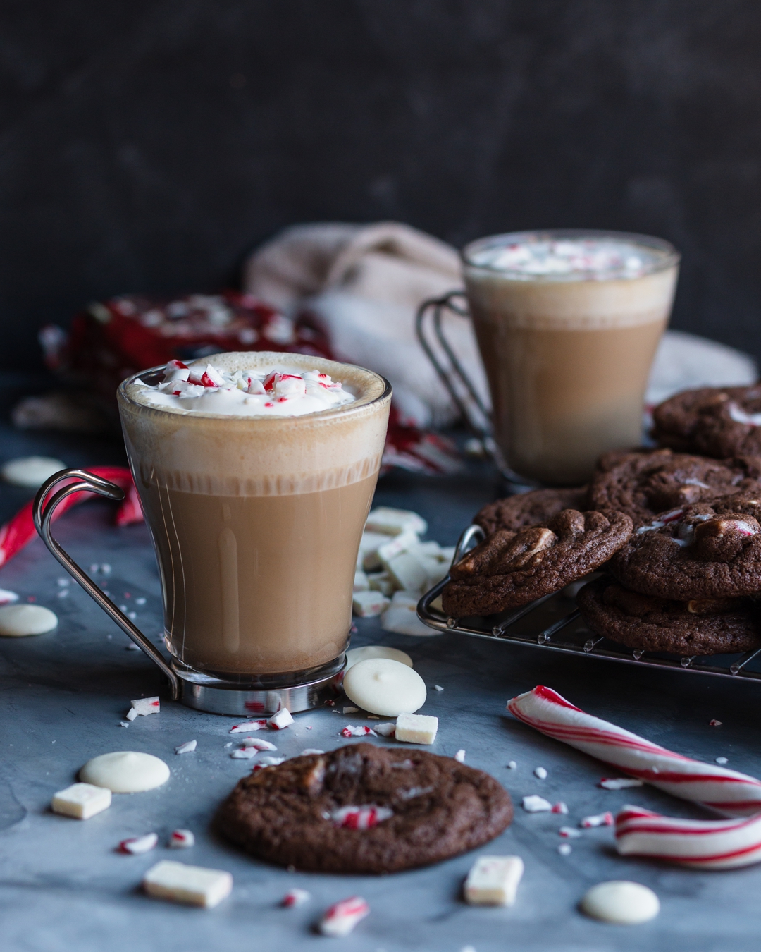 30 degree shot of a latte surrounded by cookies, candy canes, white chocolate, peppermint chips, and second latte.
