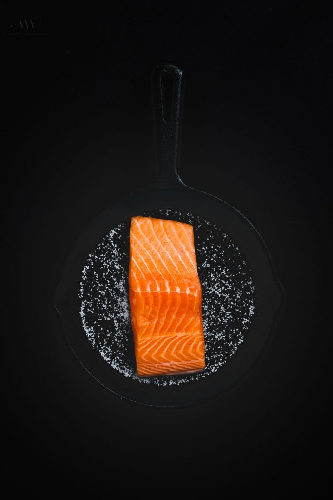 Overhead shot of raw salmon skin side down on a cast iron skillet covered with salt.