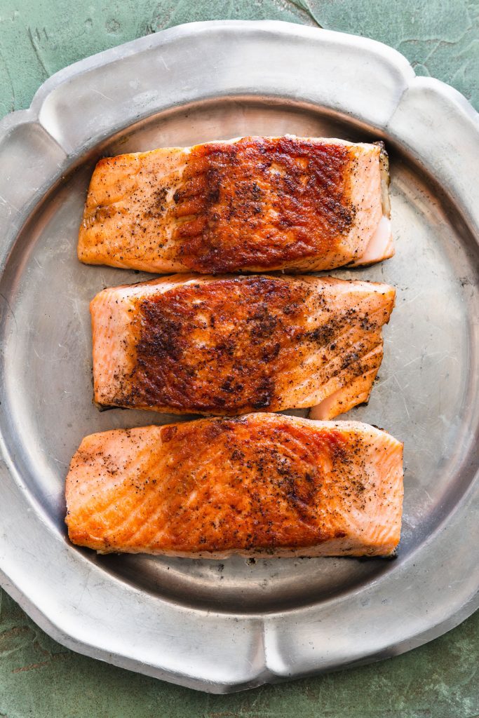 Overhead shot of three pan seared salmon fillets skin side down on a silver platter.
