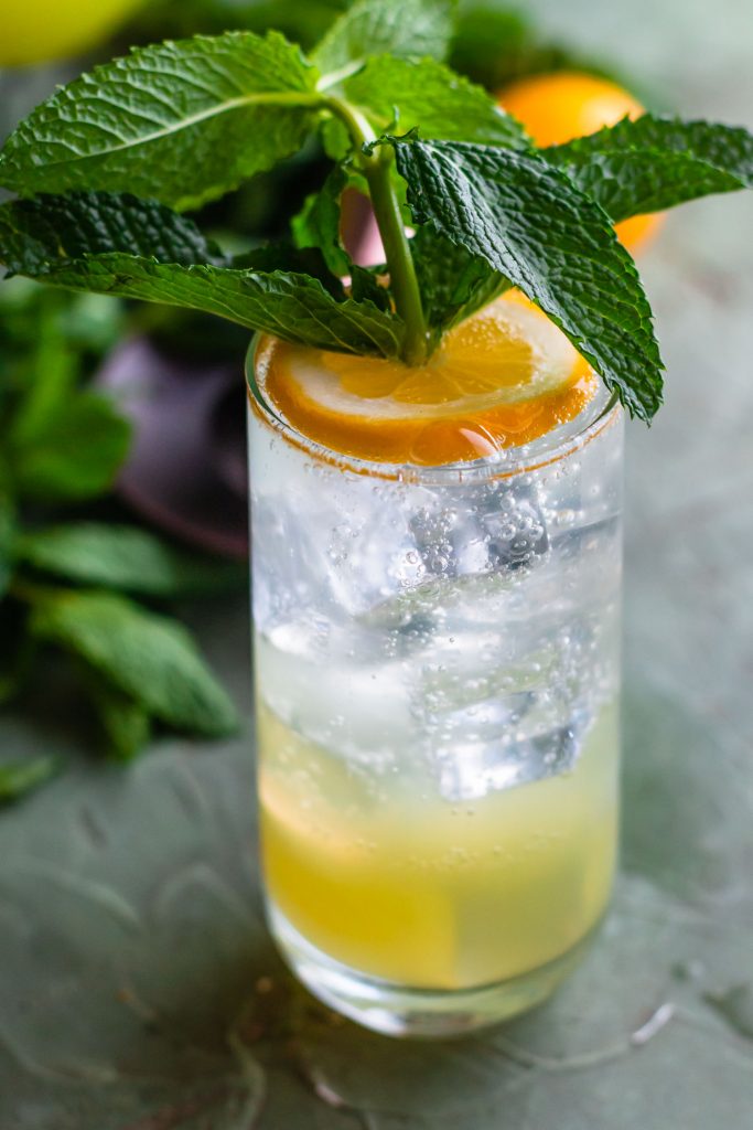 Close up side shot of a fizzy iced drink with a large mint sprig sticking out of the lemon on top.