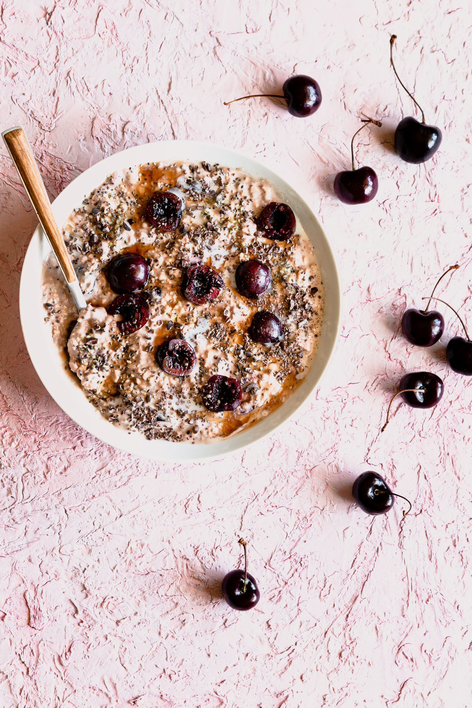 Overhead shot of Cherry Overnight Oats in a bowl with a spoon surrounded by cherries.