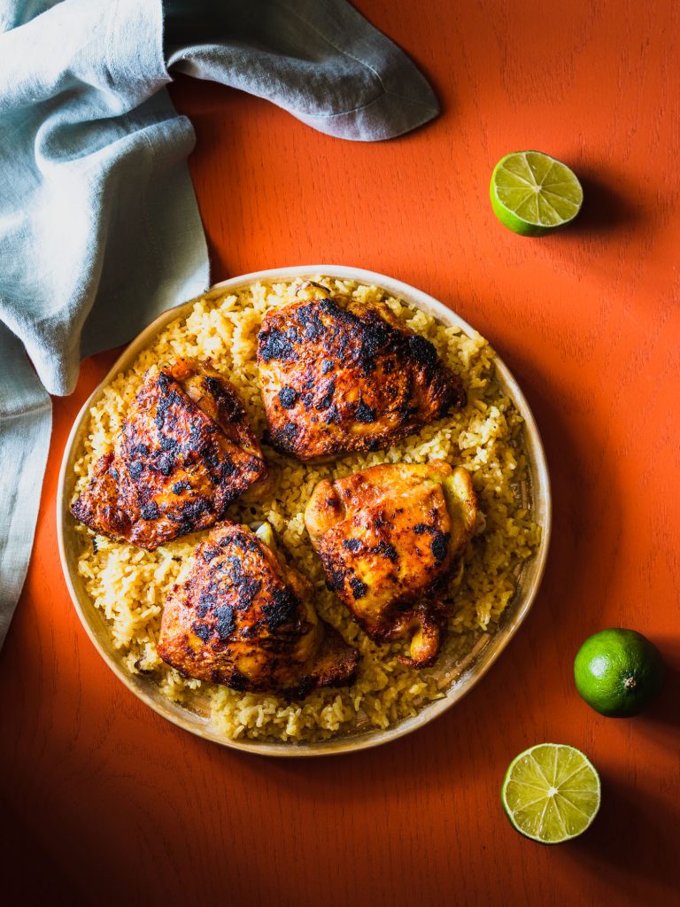 Overhead shot of rice topped with chicken thighs on a platter surrounded by limes and a napkin.