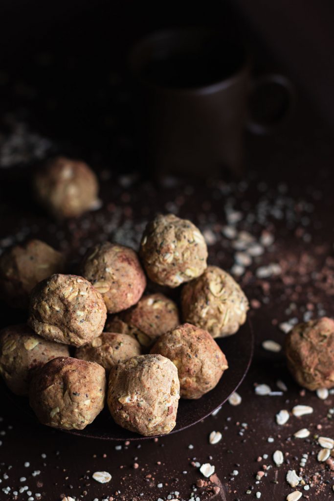 Vertical close up shot of no bake peanut butter protein balls in a small pile surrounded by oats, hemp and chia seeds, and cocoa powder.