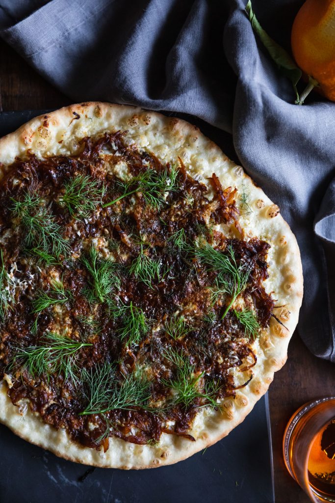 Closeup overhead shot of a Caramelized Fennel & Onion Skillet Pizza Recipe on a slate cutting board.